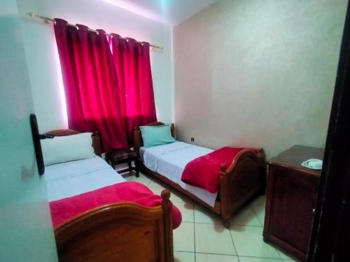 two beds in a small room with red curtains at Entire Apartment in Agadir