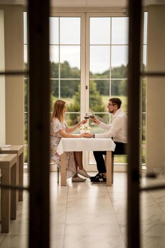 a man and woman sitting at a table drinking wine at Hotel&SPA Dwór Droblin in Leśna Podlaska
