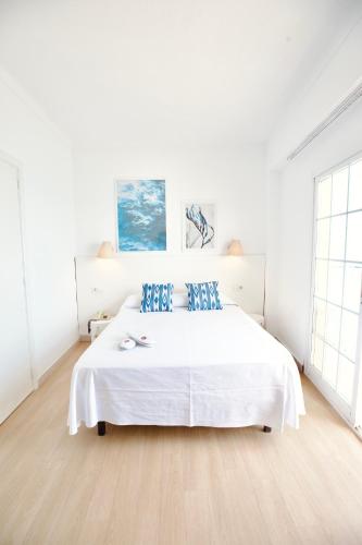 a white bedroom with a large white bed with blue pillows at JS Horitzó in Can Picafort