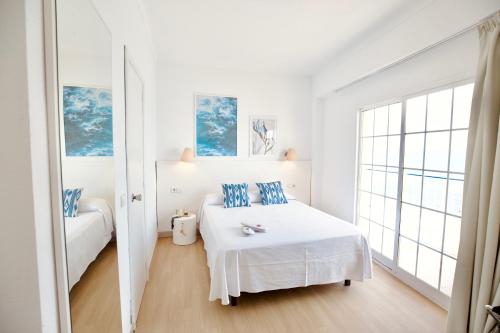a white bedroom with a bed with blue pillows at JS Horitzó in Can Picafort