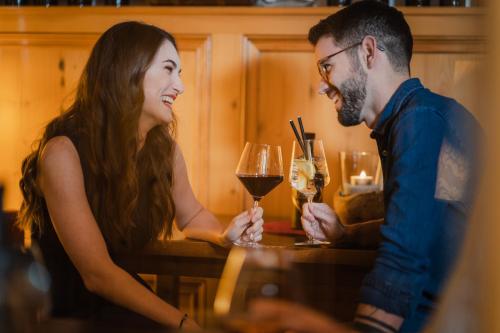 a man and woman sitting at a table with glasses of wine at Dilly - Das Nationalpark Resort in Windischgarsten