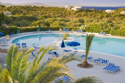 een groot zwembad met blauwe stoelen en parasols bij Hotel Cala Reale in Stintino