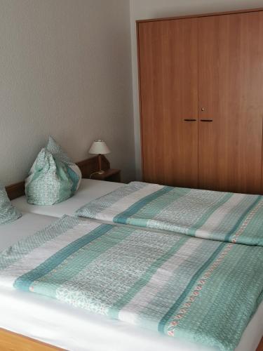 a bed with a green and white blanket and a wooden cabinet at Pension zum Park in Goldberg