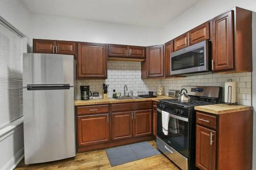 a kitchen with wooden cabinets and a stainless steel refrigerator at Chic & Fully Furnished 2BR Apartment - Roscoe 1 in Chicago