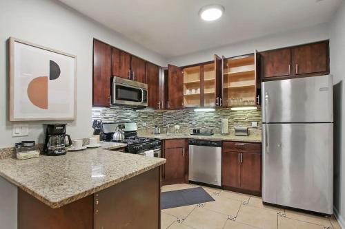 a kitchen with wooden cabinets and a stainless steel refrigerator at Modern & Furnished 2BR Apt with In-unit Laundry - Sunnyside 2E in Chicago