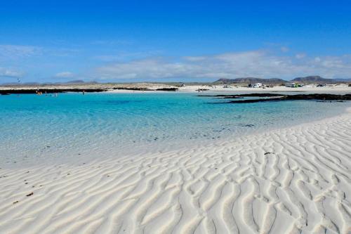 een strand met blauw water en wit zand en een pier bij Casa Alfred, El Cotillo, Best one beach to 150 m WIFI fiber in Cotillo