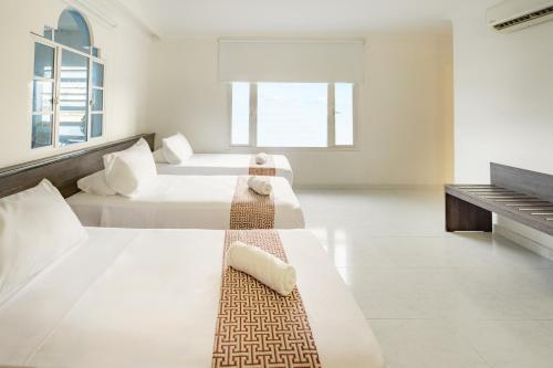 two beds in a white room with a piano at Hotel Americas San Andres Islas Colombia in San Andrés