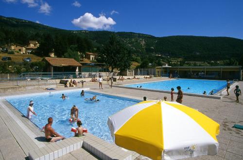 una piscina con una sombrilla blanca y amarilla en VVF Drôme Provence, en Montbrun-les-Bains