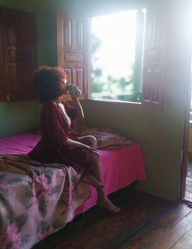a woman sitting on a bed drinking from a bottle at recanto rios Belém in Mosqueiro