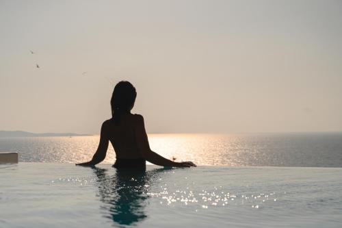 Villa Sunset Aura - Amazing Sea & Sunset View في Klouvas: امرأة جالسة في مسبح لا نهاية له تطل على المحيط
