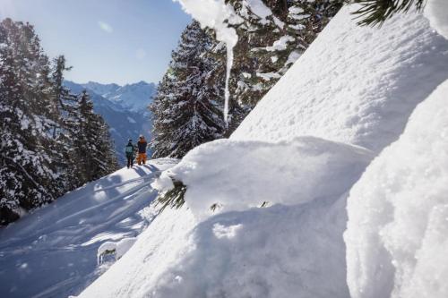 two people walking down a snow covered slope with trees at ZWEITE HEIMAT - Alpine Garden Retreat in Zillertal, presented by AlpenLuxus in Fügen