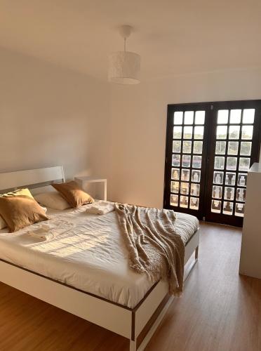a bedroom with a bed with white sheets and two windows at Nina's Stay Hostel in Charneca