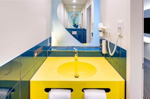 prizeotel Dortmund-City في دورتموند: حمام مع مغسلة صفراء ومرآة