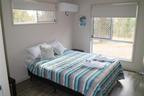 a bedroom with a bed with a striped blanket and two windows at Honeybee Wellness Resort in Kandanga