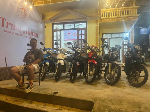 Un uomo seduto di fronte a una fila di motociclette di Trust House ( Hostel and Motobike Rental ) a Bản Tùy