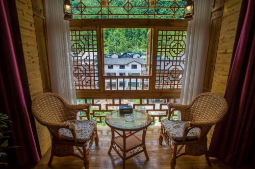Habitación con mesa de cristal, 2 sillas y ventana. en Mountain View Guesthouse en Zhangjiajie