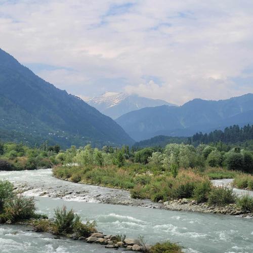 a river with a snow covered mountain in the background at White Water Resorts in Pahalgām