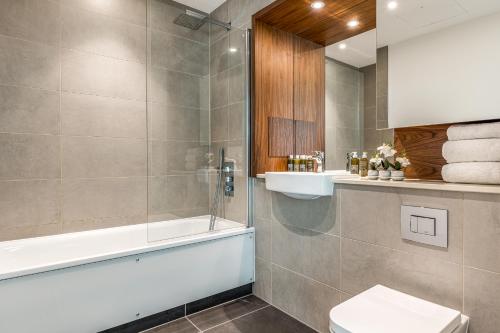 a bathroom with a shower and a toilet and a tub at Urban Rest Canary Wharf Apartments in London