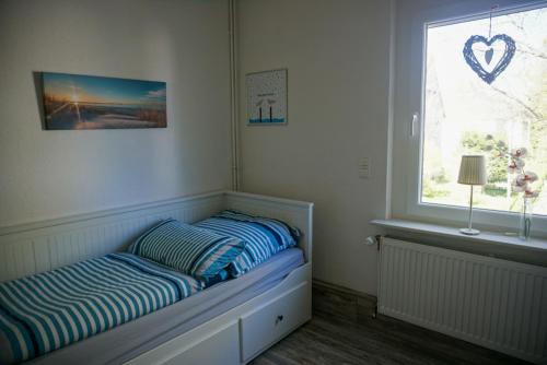 ein Schlafzimmer mit einem Bett mit gestreiften Kissen und einem Fenster in der Unterkunft Dat Wittsche Hus - Ferienwohnung an der Nordsee in Wilhelmshaven