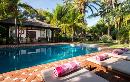 a pool with two chaise lounges next to a house at Villa in a palm tree plantation in Marbella