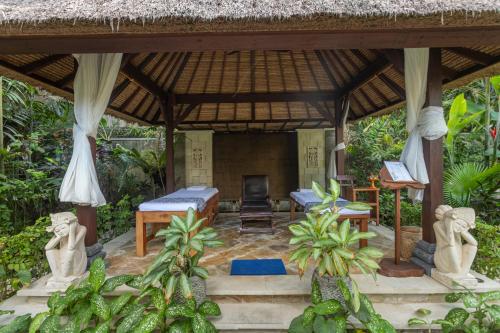 a pavilion with a bed and a chair in a garden at Nusa Indah Candidasa in Candidasa