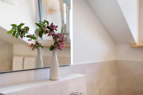 two white vases with flowers on a shelf in a bathroom at Ferienwohnung Wendelsteinblick in Bad Tölz