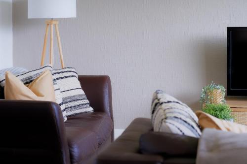 uma sala de estar com um sofá de couro castanho com almofadas em Amroth House em Cardiff