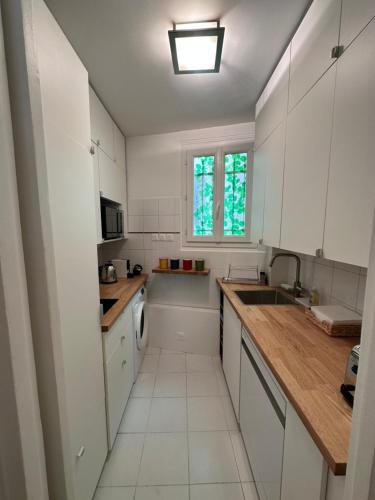 une cuisine avec des armoires blanches, un évier et une fenêtre dans l'établissement L.C. GrandTour Paris, à Paris