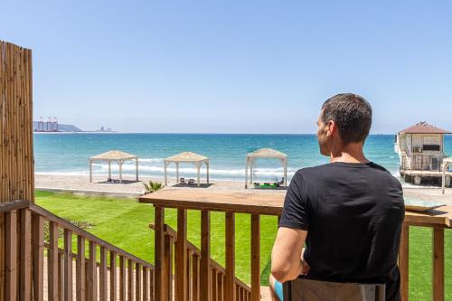 a man standing on a balcony looking at the beach at בית חוף מושלם עם גקוזי ומרפסת - Beachside Bliss W jacuzzi in Haifa