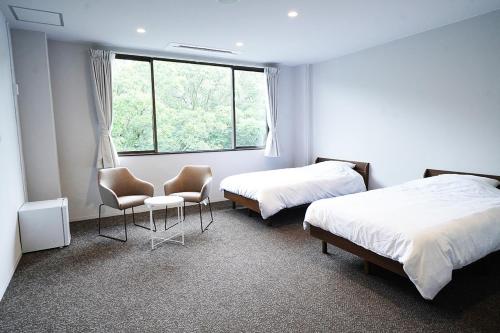 een kamer met 2 bedden, 2 stoelen en een raam bij OiseSun CAFE & HOTEL in Hyuga