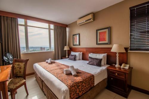 um quarto de hotel com uma cama, uma secretária e uma janela em Emakhosini Hotel On East em Durban