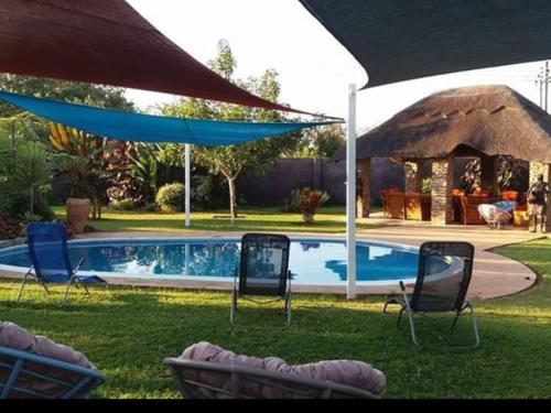 a yard with chairs and a swimming pool with an umbrella at Room in Villa - Zambezi Family Lodge - Elephant Room in Victoria Falls