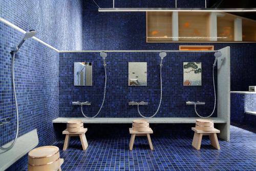 a blue tiled bathroom with two showers and stools at Azumi Setoda in Onomichi