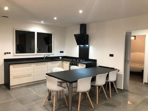 une cuisine avec une table noire et des chaises blanches dans l'établissement Location saisonnière Maen Roch, à Les Portes du Coglais