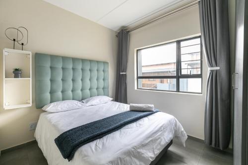 a bedroom with a bed with a blue headboard and a window at Modern 2 bed apartment, Secure estate in Midrand