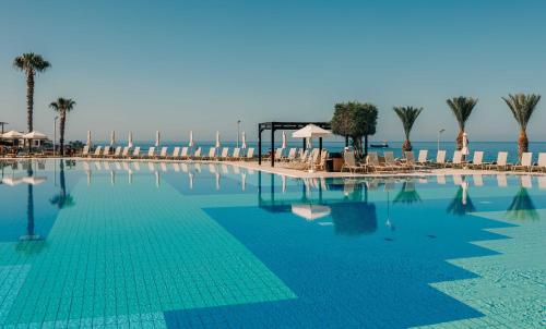 a swimming pool with chairs and palm trees and the ocean at Atlantica Akteon in Paphos City