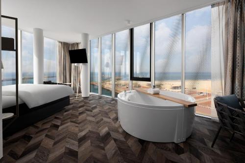 a hotel room with a tub and a bed and windows at Inntel Hotels Den Haag Marina Beach in Scheveningen