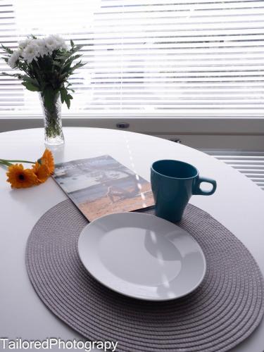 a table with a plate and a cup and a vase with flowers at Uusi asunto ydinkeskustassa, Wifi, ilmainen pysäköinti in Lappeenranta