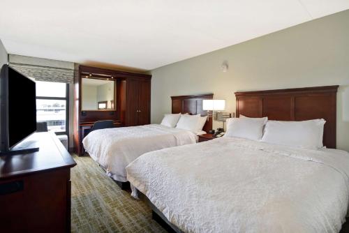 a hotel room with two beds and a flat screen tv at Hampton Inn Detroit Madison Heights South Troy in Madison Heights