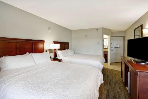 a hotel room with two beds and a flat screen tv at Hampton Inn Detroit Madison Heights South Troy in Madison Heights