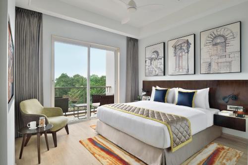 a bedroom with a large bed and a chair at Citadines Arpora Nagoa Goa in Arpora