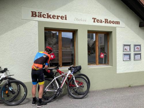 a man standing next to two bikes outside a tea room at Viosia-Ost in Fiesch