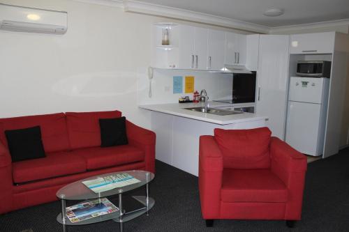 a living room with two red chairs and a kitchen at Beaches Serviced Apartments in Nelson Bay