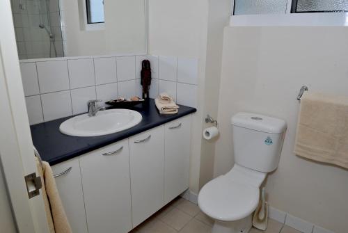 Baño blanco con lavabo y aseo en Inner city Cardona Court apartment, en Darwin