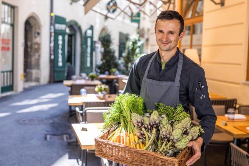 a man in an apron holding a basket of vegetables at Small Luxury Hotel Goldgasse in Salzburg