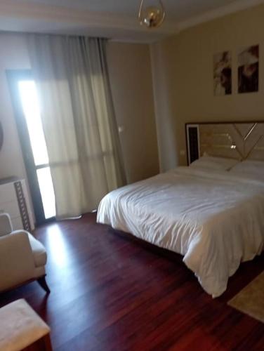 um quarto com uma cama branca e piso em madeira em بيفرلي هيلز ويست تاون الشيخ زايد em Sheikh Zayed