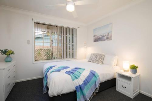 a white bedroom with a bed and a window at Tighes Hill Hideaway - Alfresco Living by the Park in Newcastle