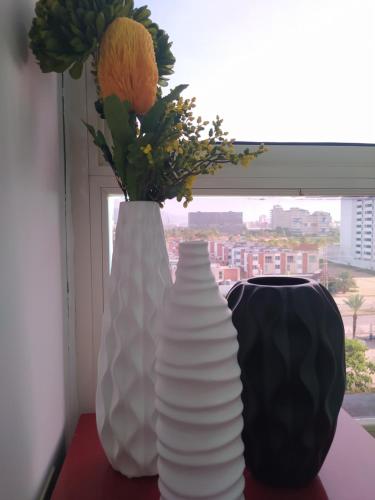 two white vases sitting on a table with flowers in a window at Margarita & More, Omas in Porlamar