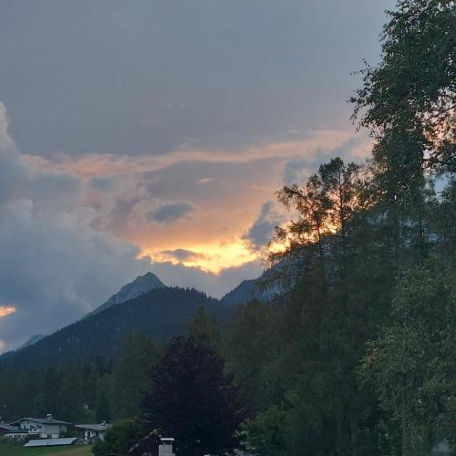 a sunset over a mountain range with trees and houses at Fewo 1 Haus am Lärchenhang in Leutasch