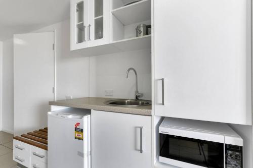 Una cocina blanca con fregadero y microondas. en Coastal Chic in Heart of Cairns with Rooftop Pool, en Cairns